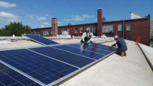Two men placing solar panels on the white barrel vault roof of the Green Garage.