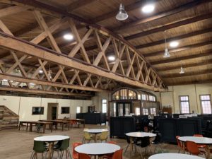 A wide view of the Green Garage interior, showcasing high wood ceilings, skylights, historic architecture and repurposed cafe furniture.