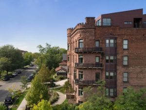 Side shot of historic El Moore, showing balconies on floors 2, 3, and 4. To the left is Alexandrine St, lined with trees. Rooftop cabins top the building.