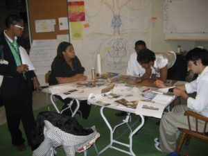 5 Detroit public school students huddled around a table, contributing design ideas.