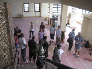 A group of visitors being led on a tour of the Green Garage during construction. The area is wide open, with no furniture, and the floors are unfinished.