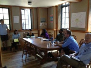 A group of 8 people sitting at a large wooden table in a conference room, participating in design work.