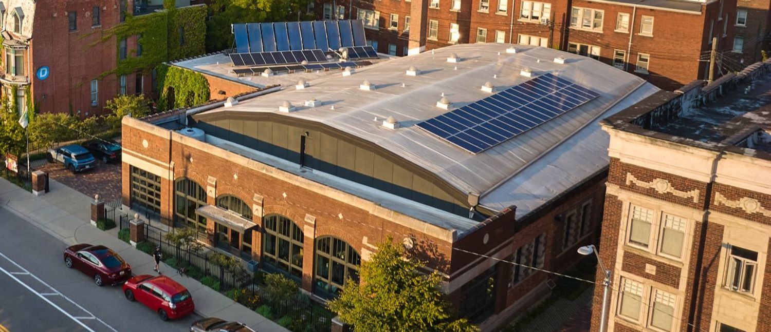 The Green Garage in its neighborhood context from above, showing the white barrel vault roof and solar panels. Other buildings shown include the Bronx Bar, apartment buildings, and Old Main, a historic building at Wayne State University.